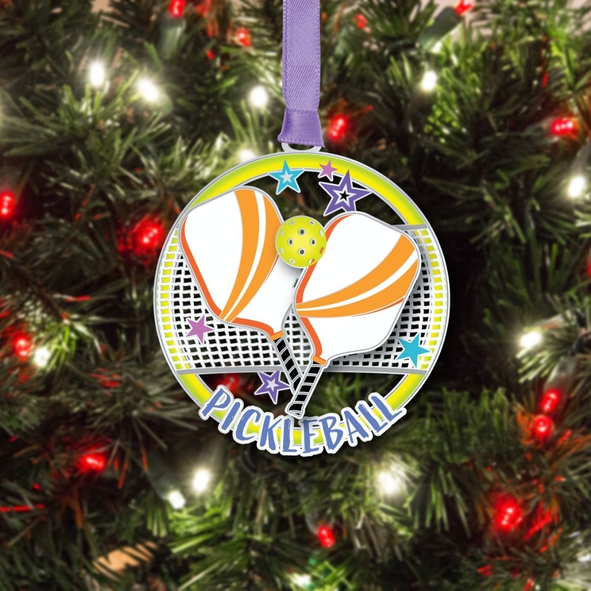 Pickleball ornament from Beacon Design hanging on a Christmas tree, featuring crossed paddles, a ball, and a net with colorful star accents.