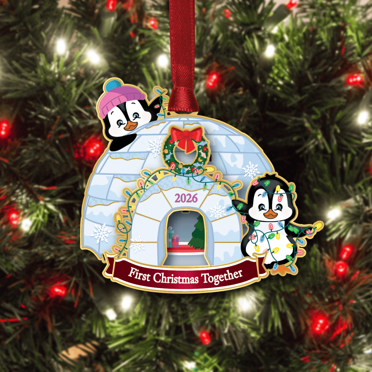 Ornament featuring a decorated igloo with two penguins, holiday lights, and the message “First Christmas Together 2026,” displayed on a decorated Christmas tree