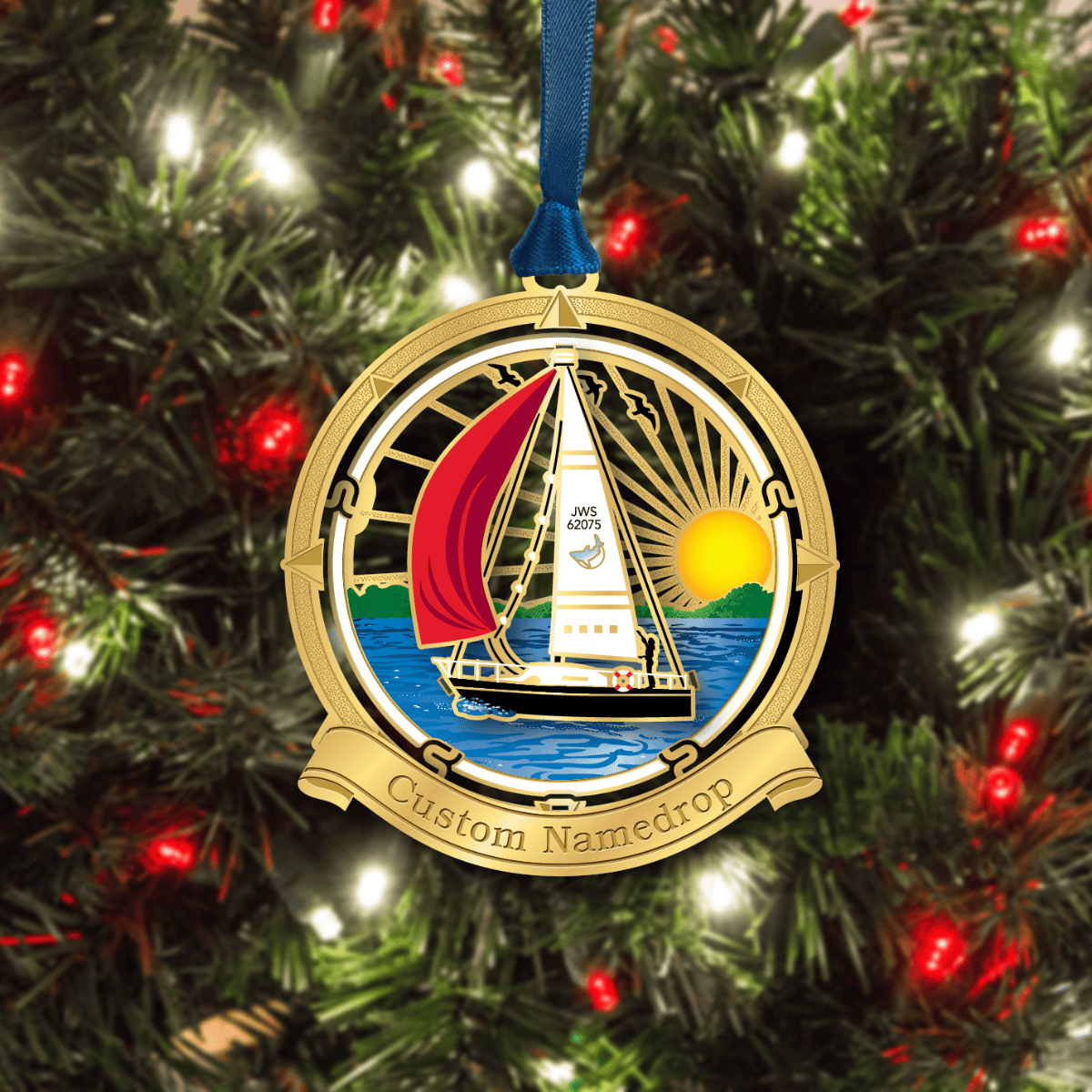 Custom namedrop ornament featuring a sailboat on open water at sunset, framed by a nautical compass design, displayed on a decorated Christmas tree