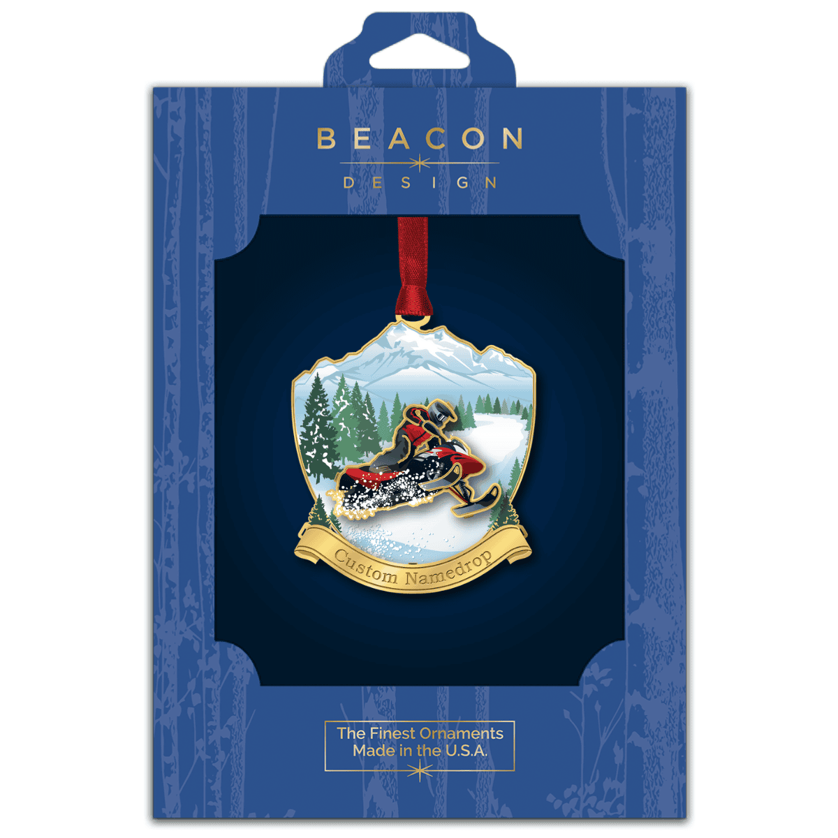 Custom namedrop ornament featuring a snowmobile rider speeding through a snowy mountain landscape with evergreen trees, displayed in Beacon Design retail packaging