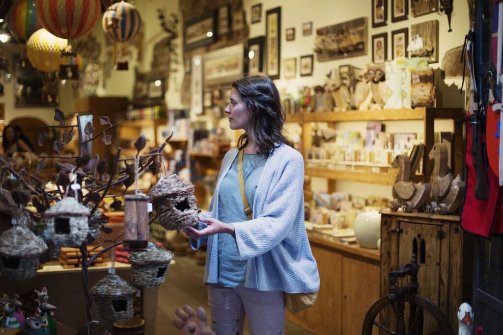 Customer browsing decorative items inside a gift shop, holding a small woven birdhouse ornament near a display stand.